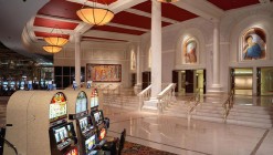 Lobby of the Colosseum showroom with casino machines in front of marble columns.