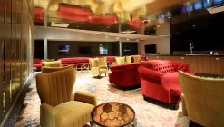 The golden ceiling in the VIP lounge reflects the red and gold tufted armchairs.
