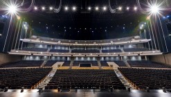 The Resorts World performance hall seen from the stage, with its black benches and walls, accented with the color champagne.