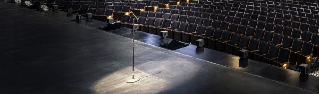 A microphone lit by a spotlight on an empty stage.